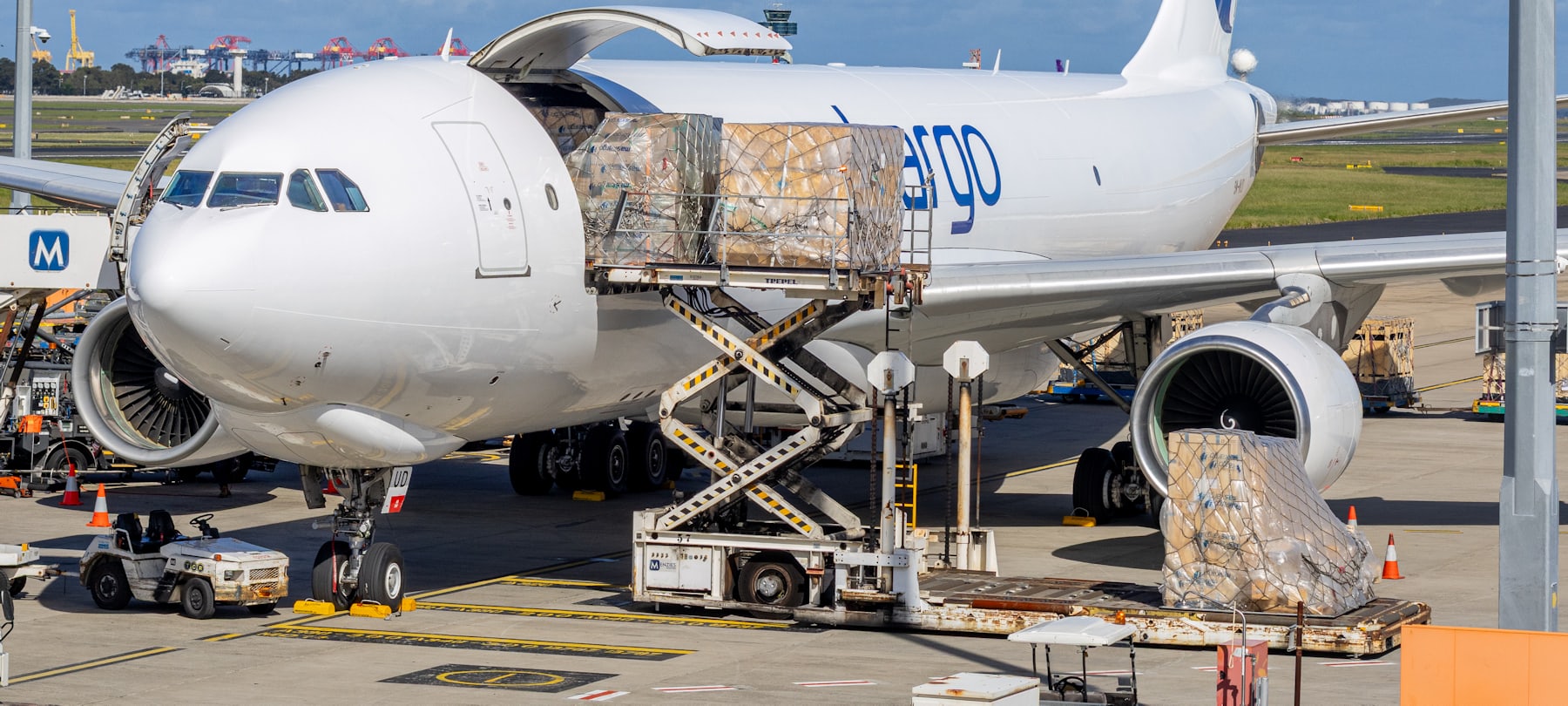 Netted air cargo pallets being loaded through the side door of a freighter aircraft, with more pallets waiting on the tarmac